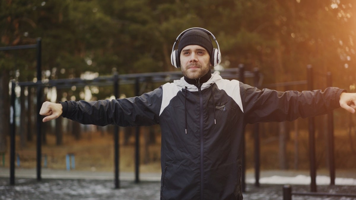 Handsome man in headphones doing warm-up exercise while listening music in winter park outdoors